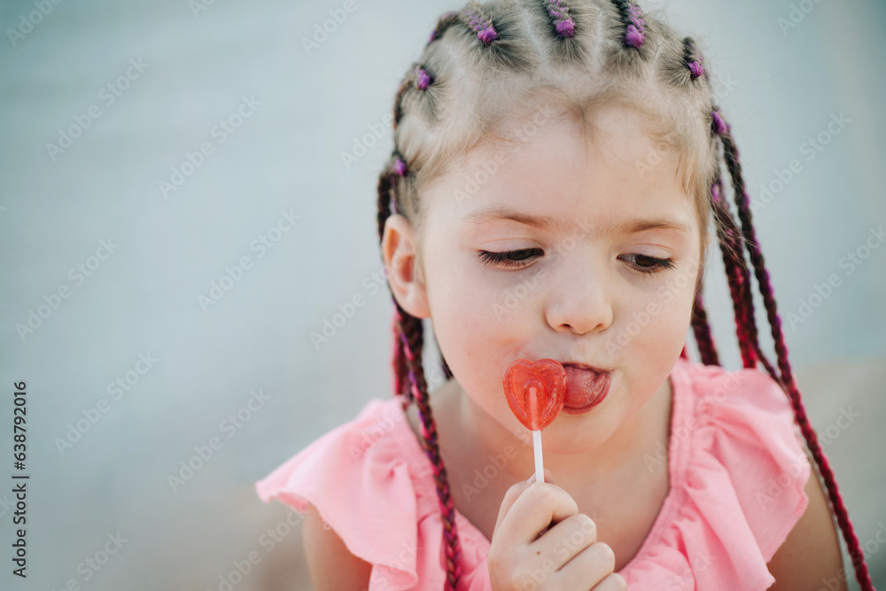 Little girl lick lollipop. Lifestyle closeup portrait of funny kids face outdoors. Summer kid outdoor portrait. Close up face of cute child. Kid having fun outdoor on sunny summer day.