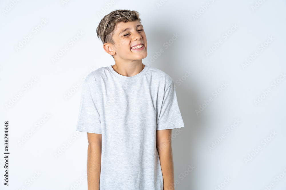 Positive Beautiful kid boy wearing grey casual t-shirt with overjoyed expression closes eyes and laughs shows white perfect teeth Positive Beautiful kid boy wearing grey casual t-shirt with overjoyed expression closes eyes and laughs shows white perfect teeth