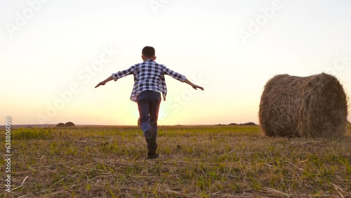A child runs through a mown meadow among sheaves of hay. The silhouette of a child at sunset. The boy runs. A child on a farm. Happy childhood, dreams of playing in nature