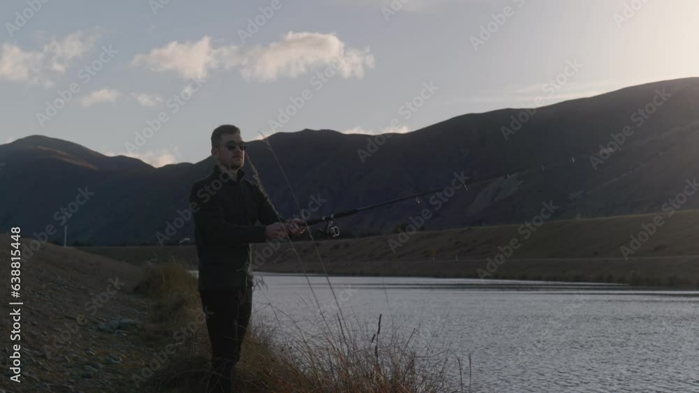 Young male fisher casting out rod into hydro canal in front of mountainous scenery Young male fisher casting out rod into hydro canal in front of mountainous scenery