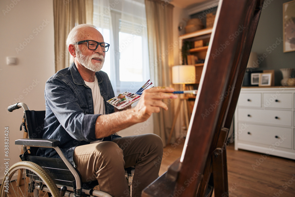Senior man in a wheelchair painting at home Senior man in a wheelchair painting at home