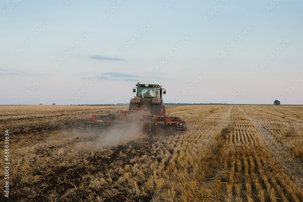 Fototapeta premium Modern tractor with a heavy trailed disc harrow works a wide hilly field. Autumn or spring agricultural campaign