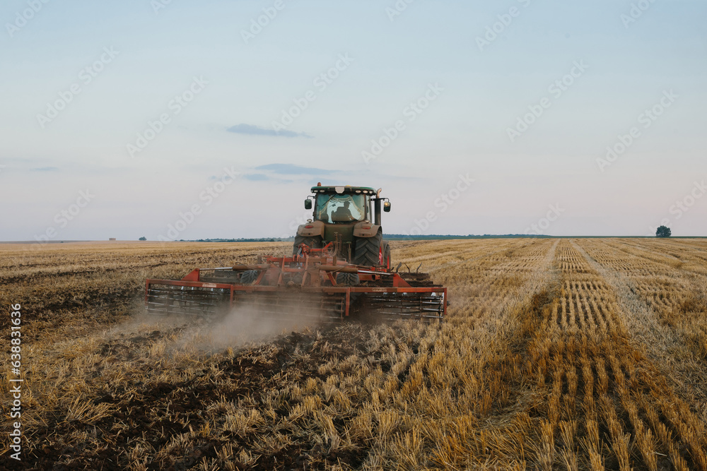 Fototapeta premium Modern tractor with a heavy trailed disc harrow works a wide hilly field. Autumn or spring agricultural campaign