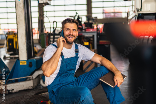 Confident mechanic sitting and talking on a smart phone in a workshop