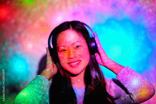 Happy Asian woman in headphones under bright illumination in stu