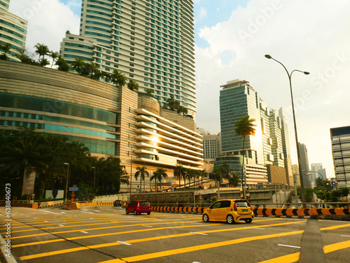A wide road in Kuala Lumpur during a sunny day with palm trees and skyscrapers in the background © Michalina