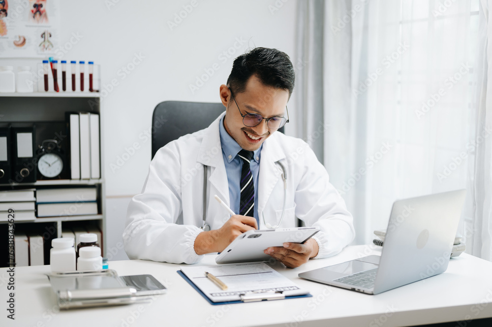 Physician doctor sit on table in hospital. Attractive therapist male practitioner pharmacist smile and use tablet and laptop. after success work from treatment Physician doctor sit on table in hospital. Attractive therapist male practitioner pharmacist smile and use tablet and laptop. after success work from treatment