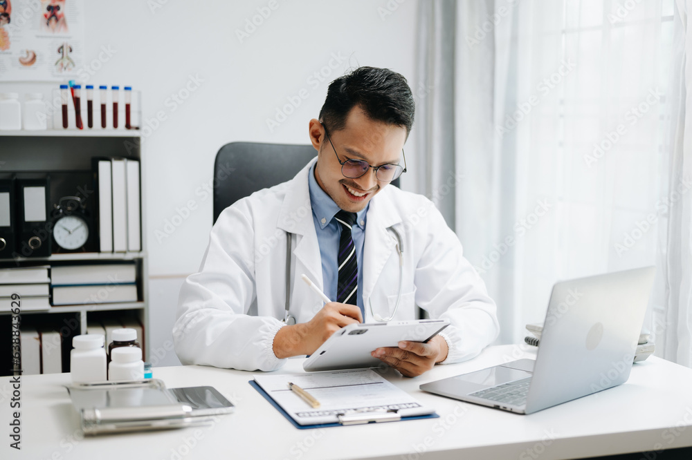 Physician doctor sit on table in hospital. Attractive therapist male practitioner pharmacist smile and use tablet and laptop. after success work from treatment