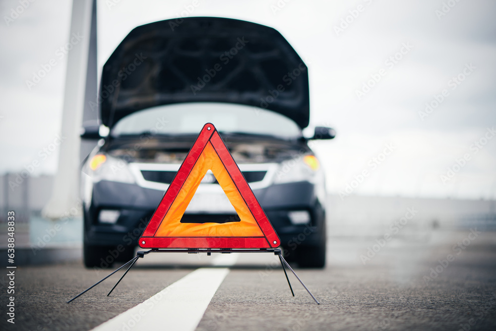 Red emergency stop sign on road. Blurred broken down car with warning