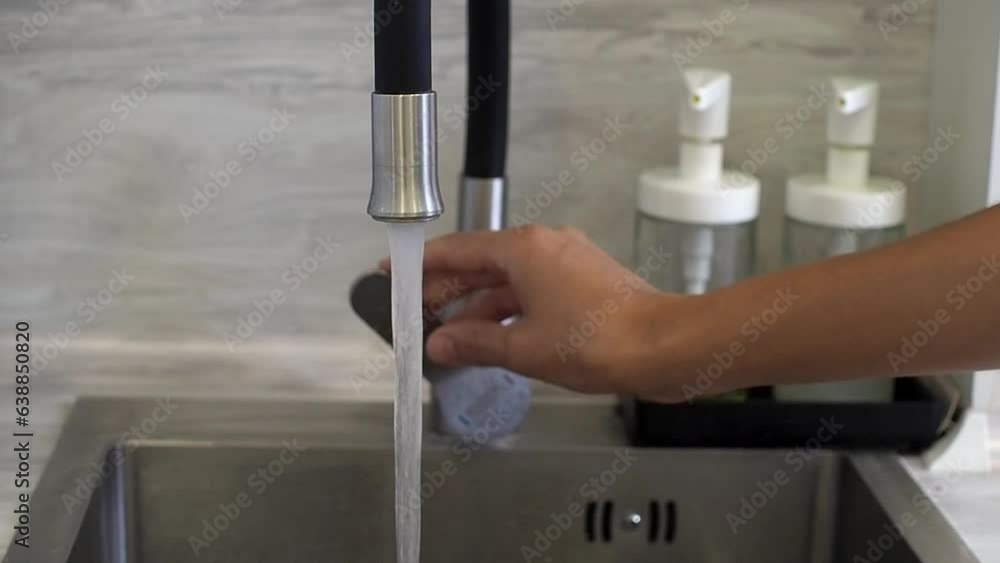 Female hand turning water tap opened. Water running from faucet in the kitchen.