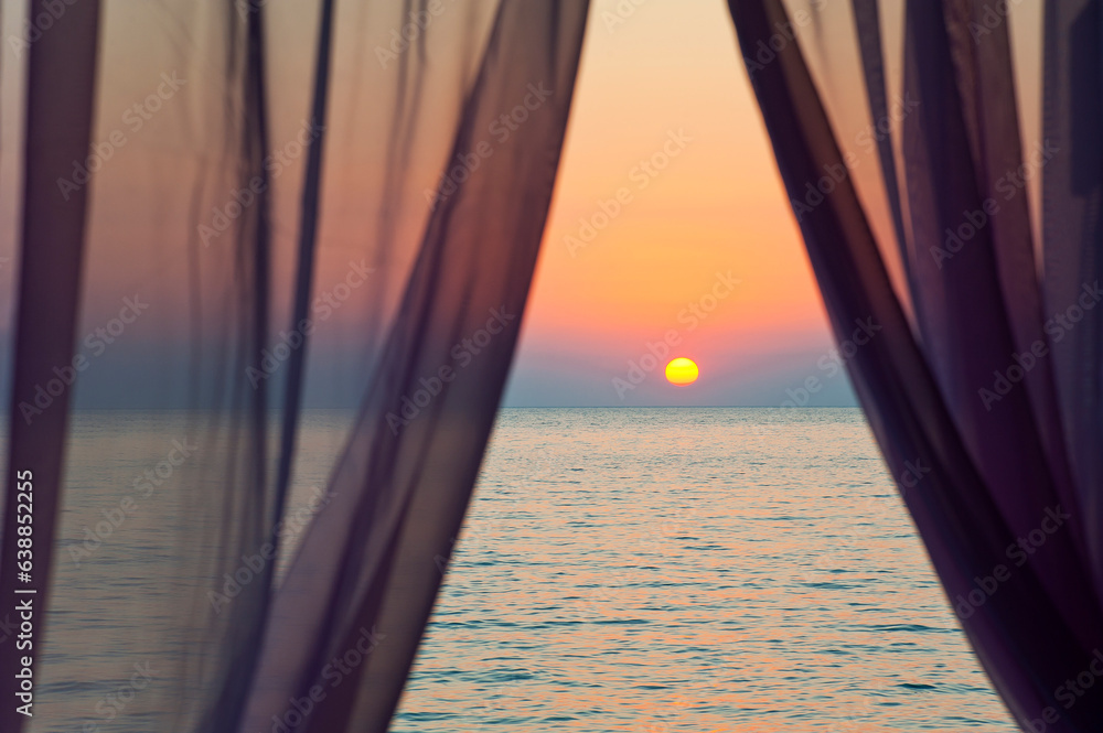 Obraz premium Sunset on a calm sea behind the window curtains.