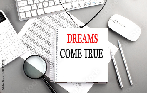 DREAMS COME TRUE text on notepad on chart with keyboard and calculator on grey background