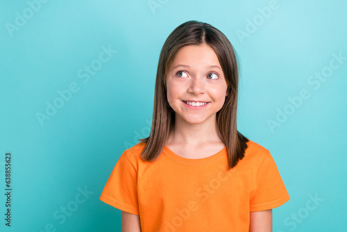 Portrait of charming cute little girl looking empty space dreaming wearing orange t-shirt isolated cyan color background © deagreez