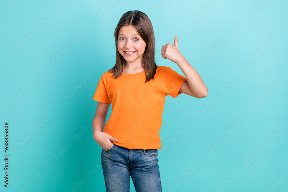 Portrait of adorable little small girl raising thumb finger up approving wearing orange t-shirt jeans isolated teal color background Portrait of adorable little small girl raising thumb finger up approving wearing orange t-shirt jeans isolated teal color background