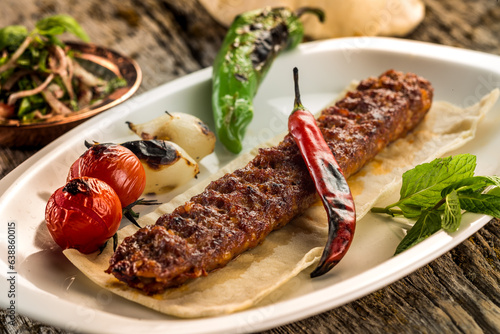 Delicious grilled Adana kebab with vegetables on a plate
wooden background