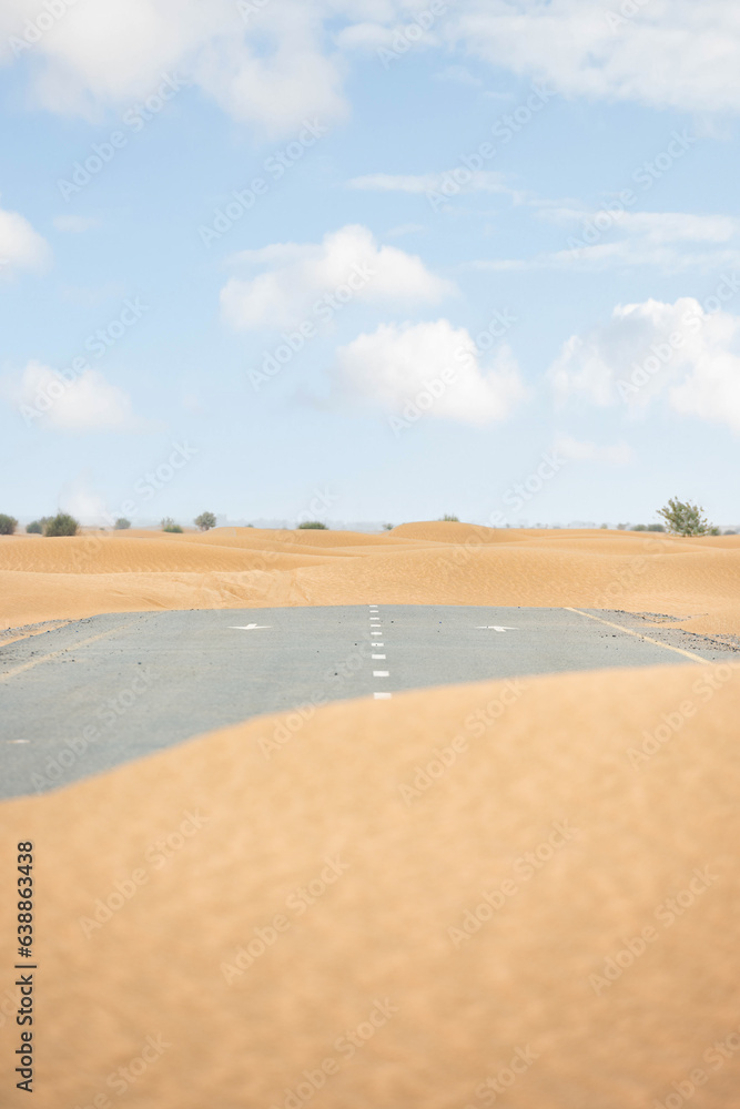 (Selective focus) Stunning view of a deserted road covered by sand dunes. Empty road that run through the Dubai desert. Dubai, United Arab Emirates, (UEA)