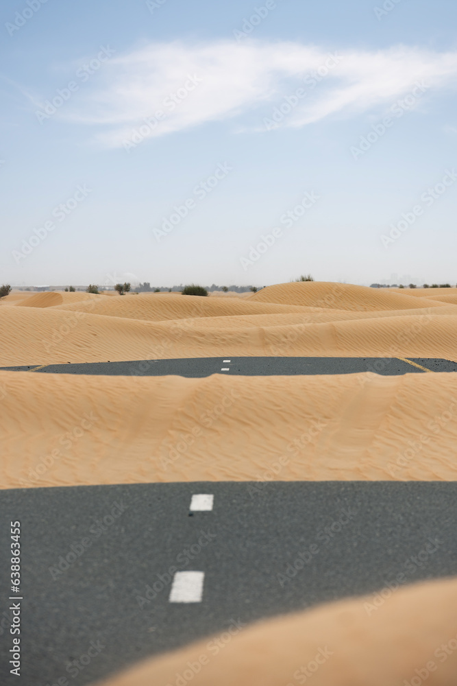 (Selective focus) Stunning view of a deserted road covered by sand dunes. Empty road that run through the Dubai desert. Dubai, United Arab Emirates, (UEA)