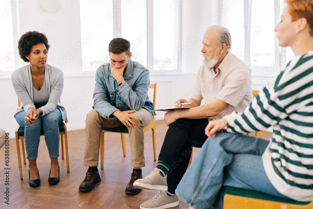 Side view of mature adult team leader speaking on therapy meeting of addicts, sharing problem, giving support to teammates. Businessman, boss talking to colleagues, sharing ideas to project staff. Side view of mature adult team leader speaking on therapy meeting of addicts, sharing problem, giving support to teammates. Businessman, boss talking to colleagues, sharing ideas to project staff.