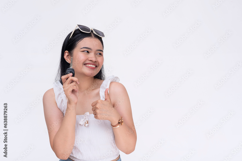 A happy young woman making a thumbs up sign while holding her car keys. A new driver smiling looking to the right. Isolated on a white background.