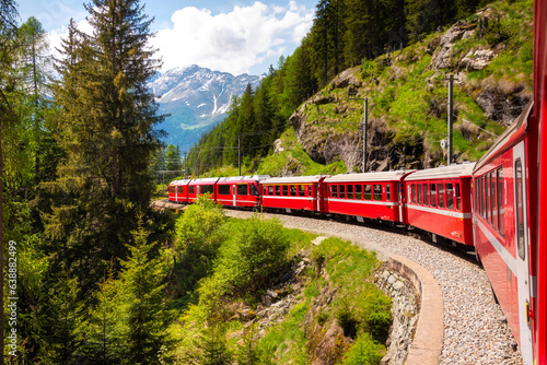 Red train moving in beautiful green summer forest in Switzerland