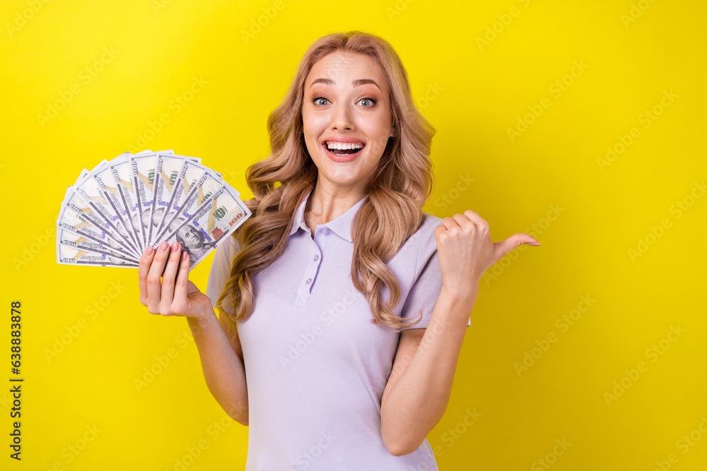 Photo of cute excited woman dressed violet t-shirt showing dollars fan thumb empty space isolated yellow color background Photo of cute excited woman dressed violet t-shirt showing dollars fan thumb empty space isolated yellow color background