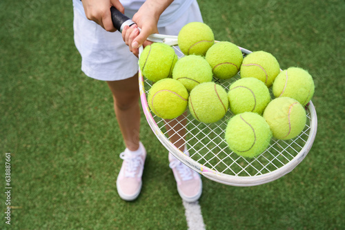 Girl holds a lot of yellow balls on tennis racket