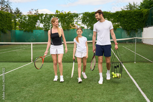Dad, mom and teenage daughter are walking along tennis court