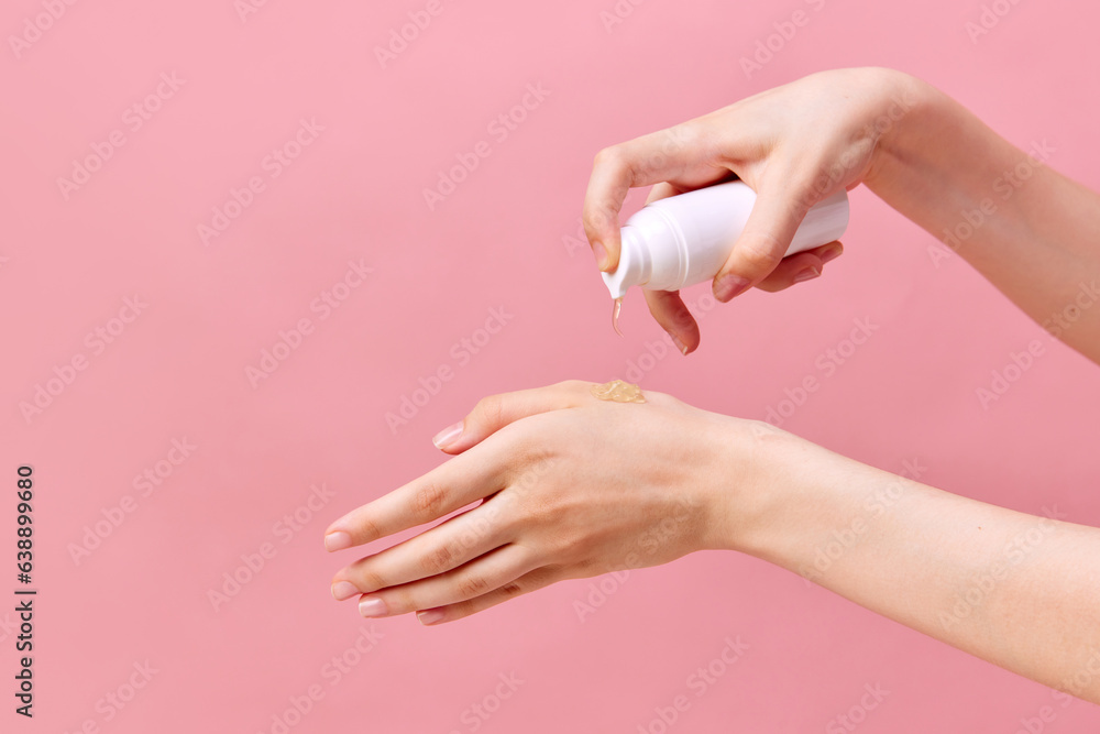 Naklejka premium Woman's hand squeezing cream, gel for hands from unmarked bottle with dispenser. Close-up, pastel pink background. Concept of body care.
