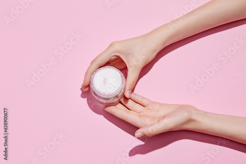 Top view of young tender woman s hands holding open jars of cosmetic creams on pink background. Female face care.