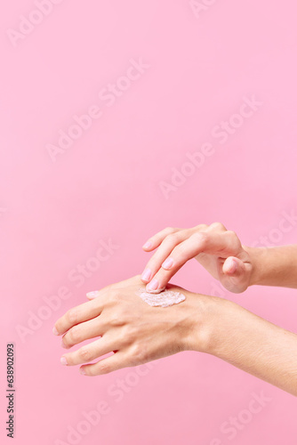 Beautiful young woman hands applying cream on her hands on pastel pink background.