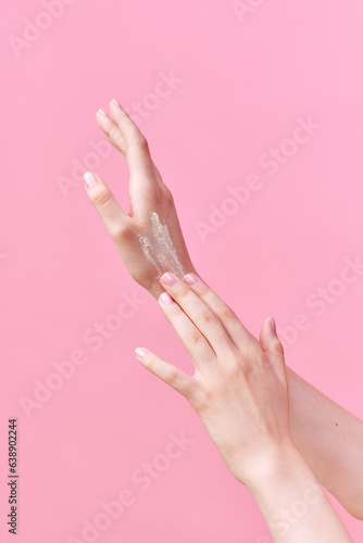 Cropped image of beautiful young woman hands applying cream, scrub on her hands on pastel pink background. © Lustre Art Group 