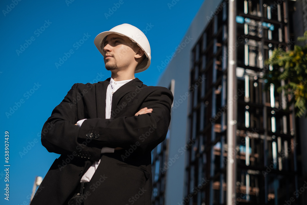 Fototapeta premium male foreman at a construction site looks at the quality of work, Architectural design holds a laptop at a construction site, checks plans. Successful engineer or architect, cheerful businessman.