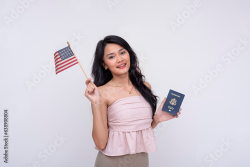 A happy asian woman proudly shows her newly acquired US passport while waving the American flag. A naturalized or second generation citizen.Isolated on a white background. photo