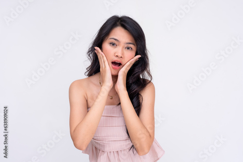 A surprised young asian woman gasps looking shocked, both hands placed on her cheeks. A startling revelation. Isolated on a white background.