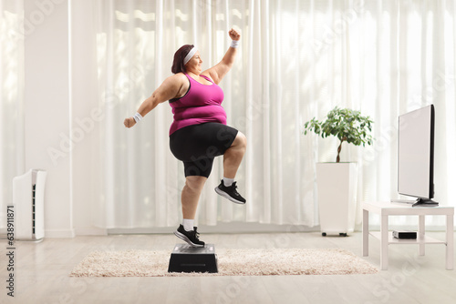 Overweight woman watching tv and exercising step aerobics