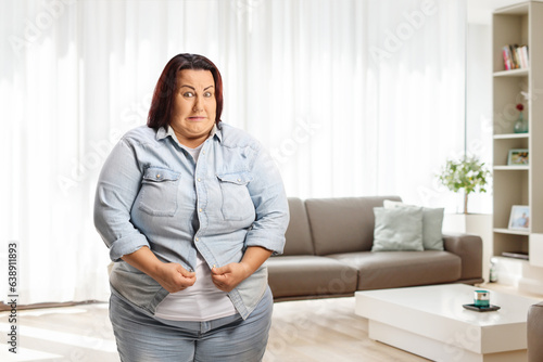 Young overweight woman at home trying to button a shirt