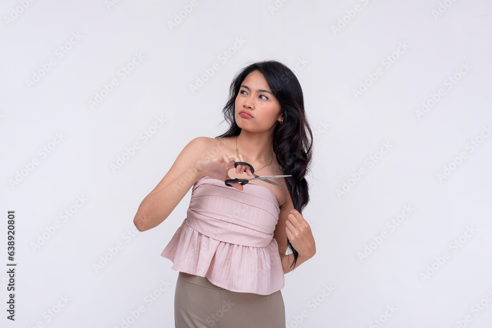 An undecided woman contemplates cutting her hair with a pair of scissors for a shorter hairstyle. Isolated on a white background. An undecided woman contemplates cutting her hair with a pair of scissors for a shorter hairstyle. Isolated on a white background.