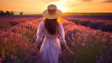 Happy caucasian woman with long hair and a hat walking through in purple lavender flowers field
