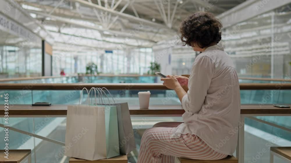 Shopping mall, Stylish woman Relaxed Works with touch smartphone holds phone in hands In entertainment center, concept Modern fashionista Spends free time in the store.glass of coffee Shopping mall, Stylish woman Relaxed Works with touch smartphone holds phone in hands In entertainment center, concept Modern fashionista Spends free time in the store.glass of coffee