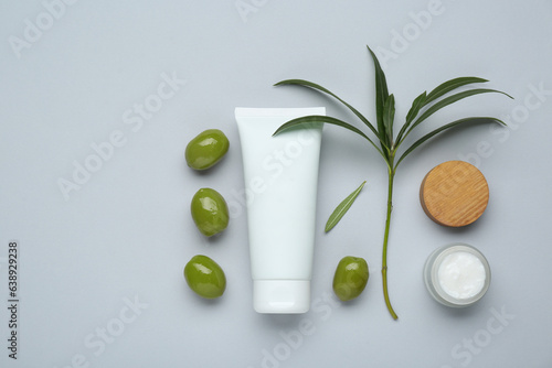 Cosmetic products with olive essential oil on light grey background, flat lay