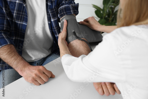 Doctor measuring blood pressure of man at table indoors  closeup
