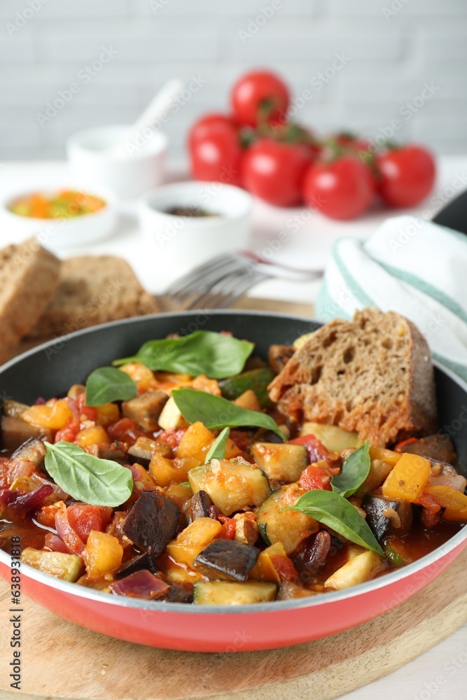 Dish with tasty ratatouille, bread and basil on wooden board, closeup