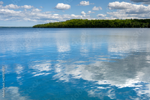 Glassy water reflecting blue sky and white clouds over a peaceful lake in Canada