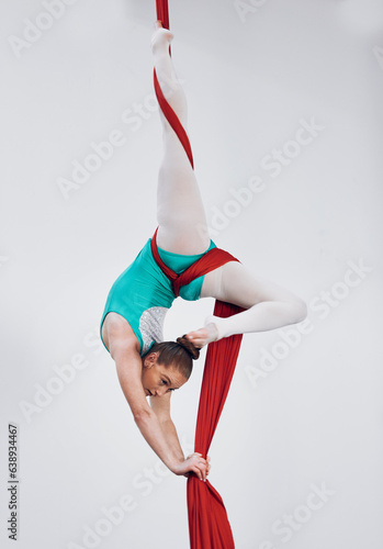 Gymnastics, aerial acrobat and silk with a woman in air for performance, sports and balance. Young athlete person or gymnast hanging on red fabric and white background with space, art and creativity