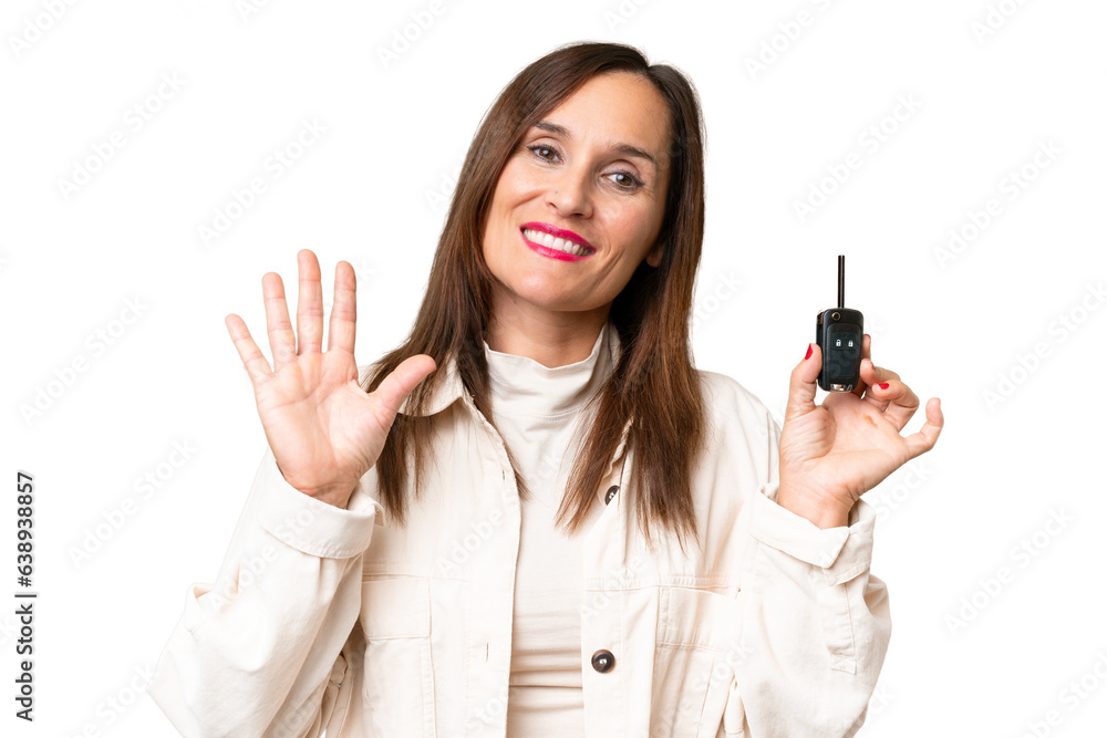 Middle-aged woman holding car keys over isolated background saluting with hand with happy expression Middle-aged woman holding car keys over isolated background saluting with hand with happy expression