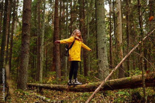 Female tourist in a yellow coat with a backpack traveling along a wooden path in the forest. Trekking trail. Concept of travel, nature, vacation.