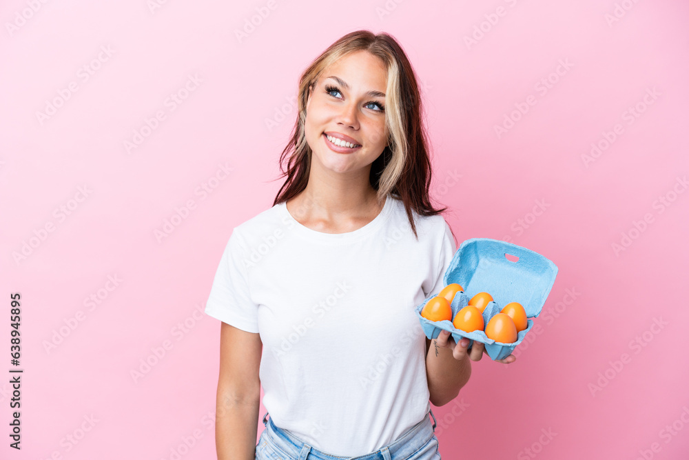 Young Russian woman holding eggs isolated on pink background thinking an idea while looking up Young Russian woman holding eggs isolated on pink background thinking an idea while looking up
