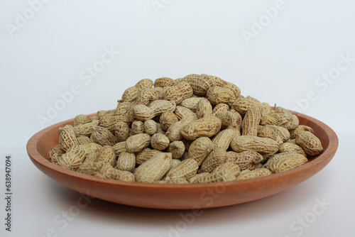 Groundnut, Goober or Monkey Nut, or Arachis hypogaea, on a wooden plate, isolated in white background. Ready to eat as snack photo