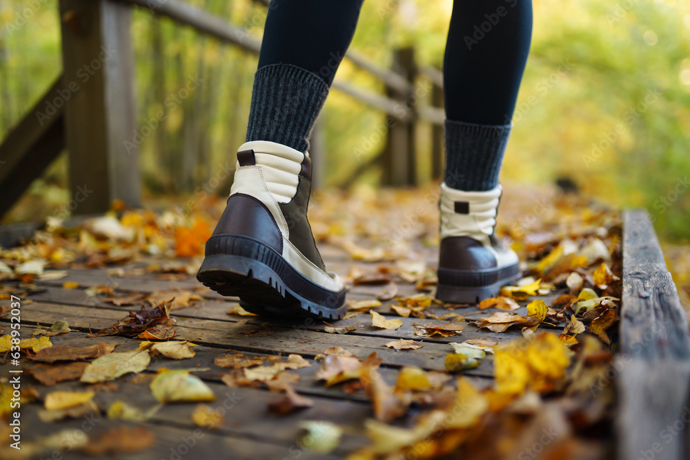Women's feet in boots go along a wooden walking path in the autumn forest. Vacation travel concept, hiking trail