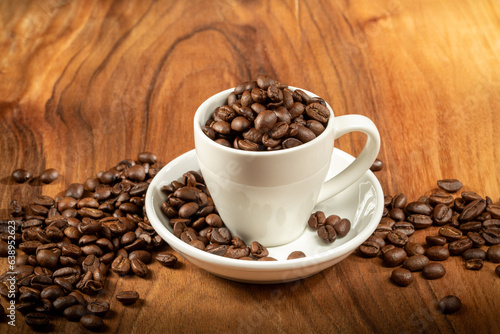 Coffee theme. A ceramic cup filled to the brim with coffee beans stands on a wooden background